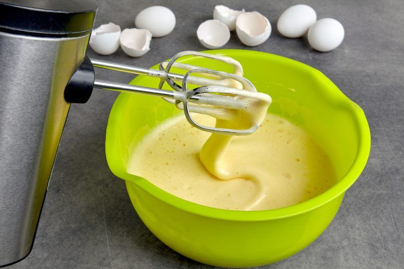 Beaten eggs with sugar and flour in a green bowl and a mixer